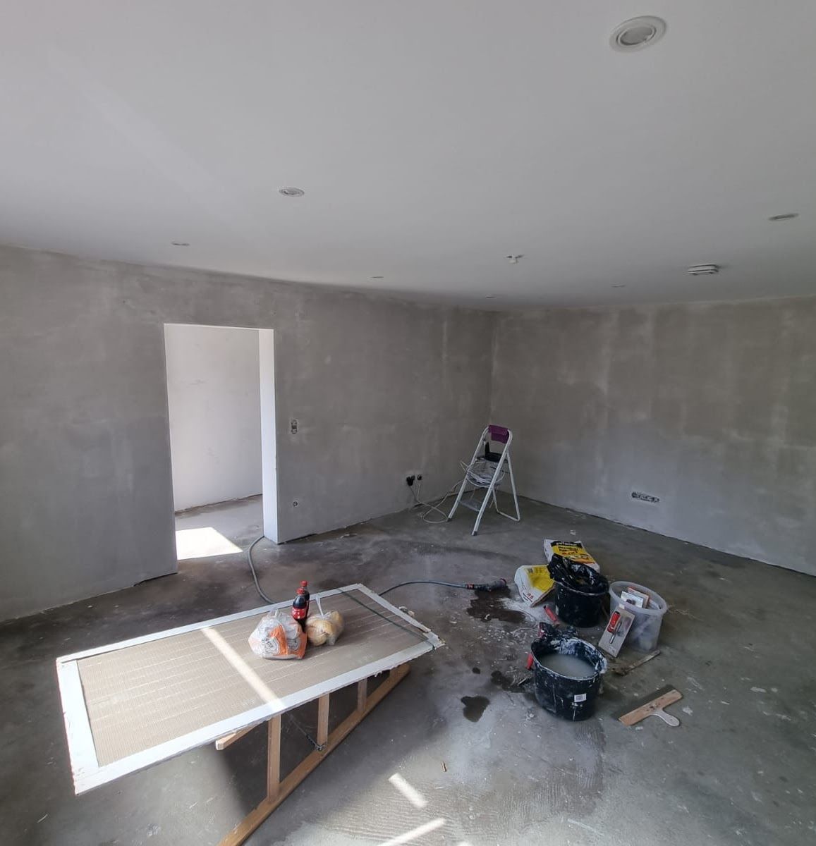 Raum im Umbau, kahle Wände, Werkzeug, Leiter, Tisch mit Gegenständen.