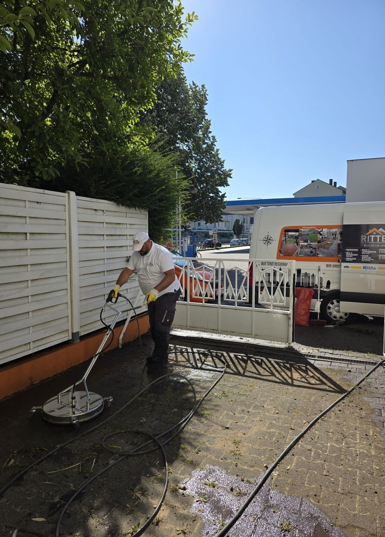 An einem sonnigen Tag reinigt ein Mann mit einem Hochdruckreiniger eine Betonfläche bzw. eine Einfahrt.