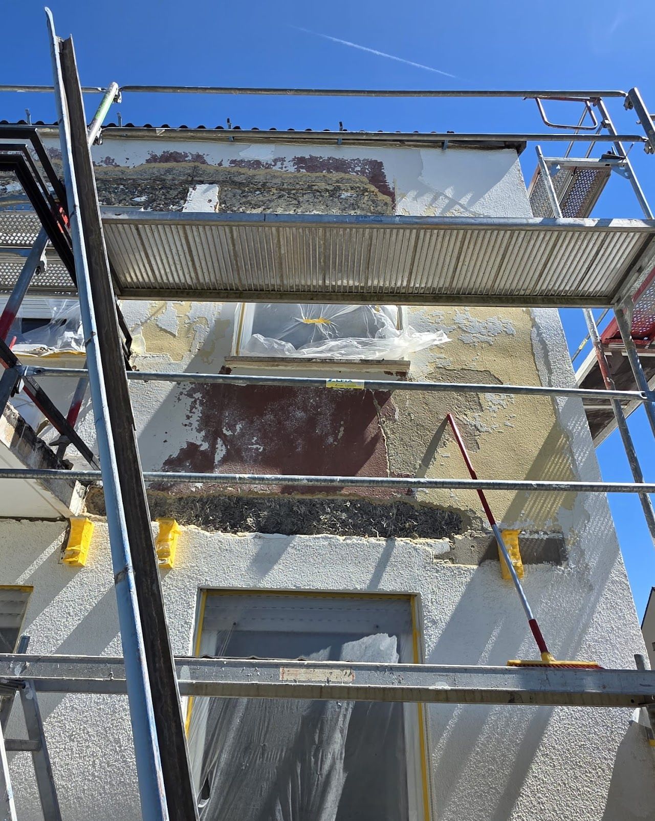 Gerüst an einem Gebäude mit abblätternder Farbe; Außenarbeiten im Gange an einem sonnigen Tag.