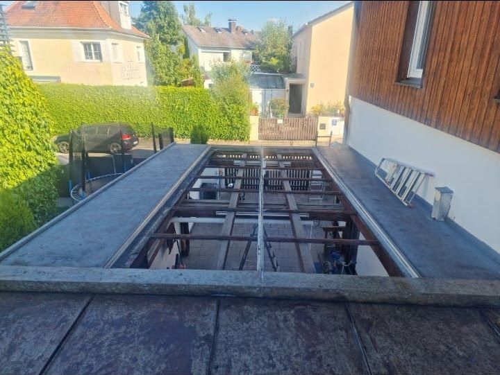Blick auf ein teilweise errichtetes Flachdach über einer Terrasse mit Metallrahmen und dunklem Dachmaterial.