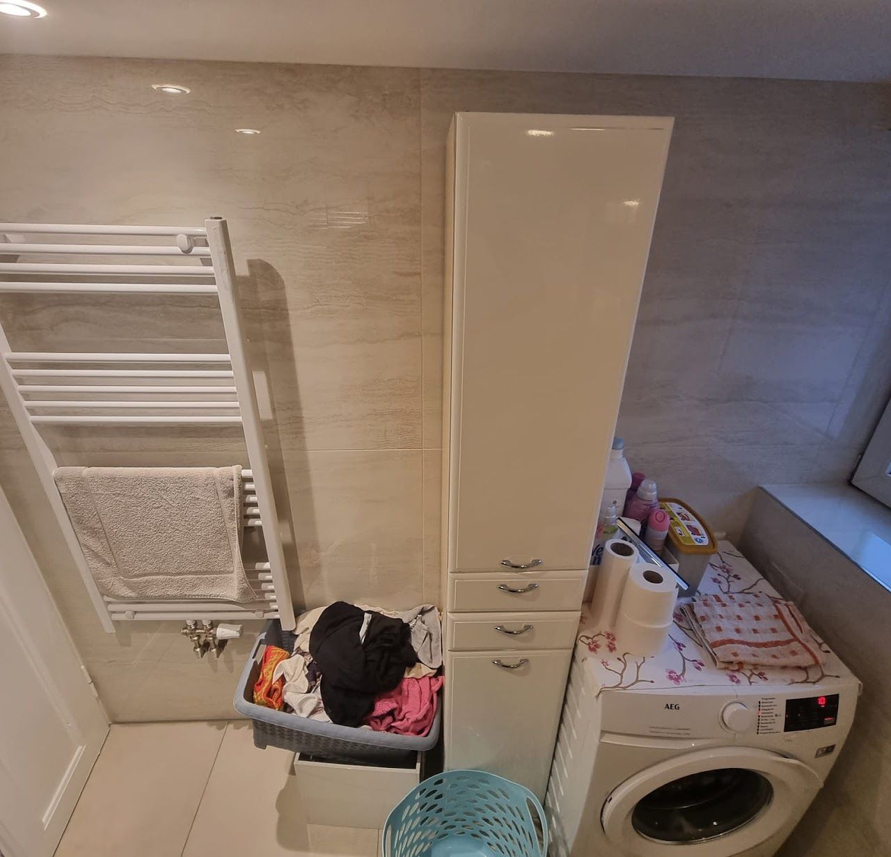 Badezimmer mit einem hohen weißen Schrank, einer Waschmaschine und einem Handtuchhalter.