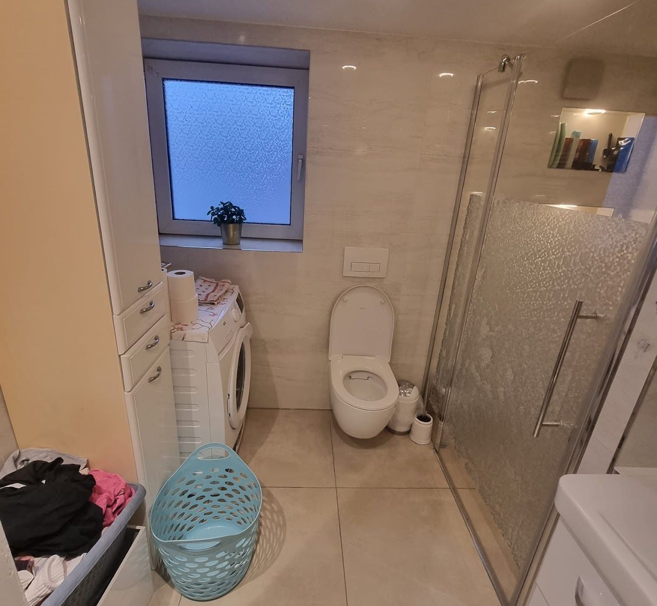 Badezimmer mit Toilette, Dusche, Waschmaschine und Fenster.