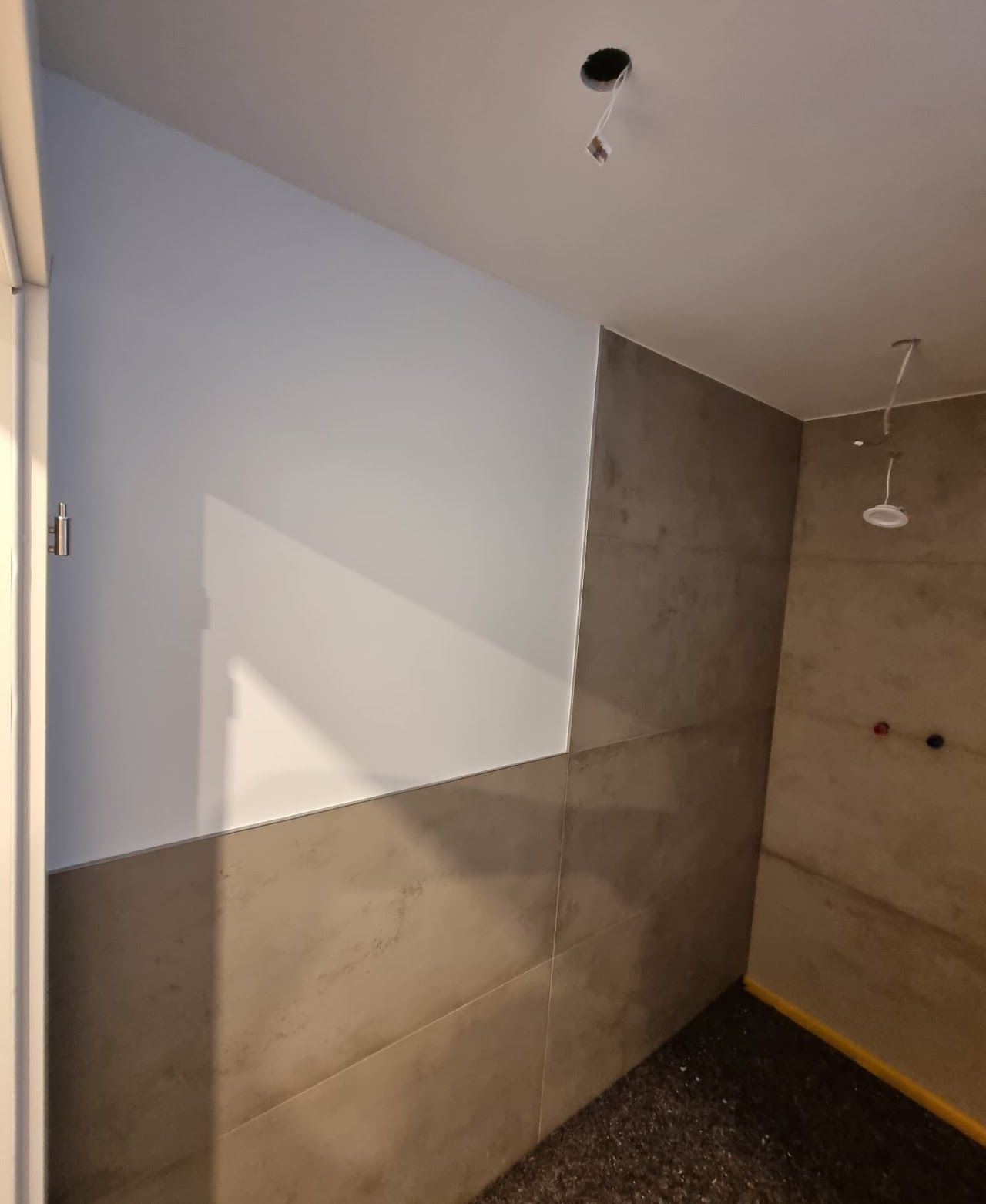 Badezimmer mit grau gefliesten Wänden und einer weiß gestrichenen oberen Wand; unfertig.