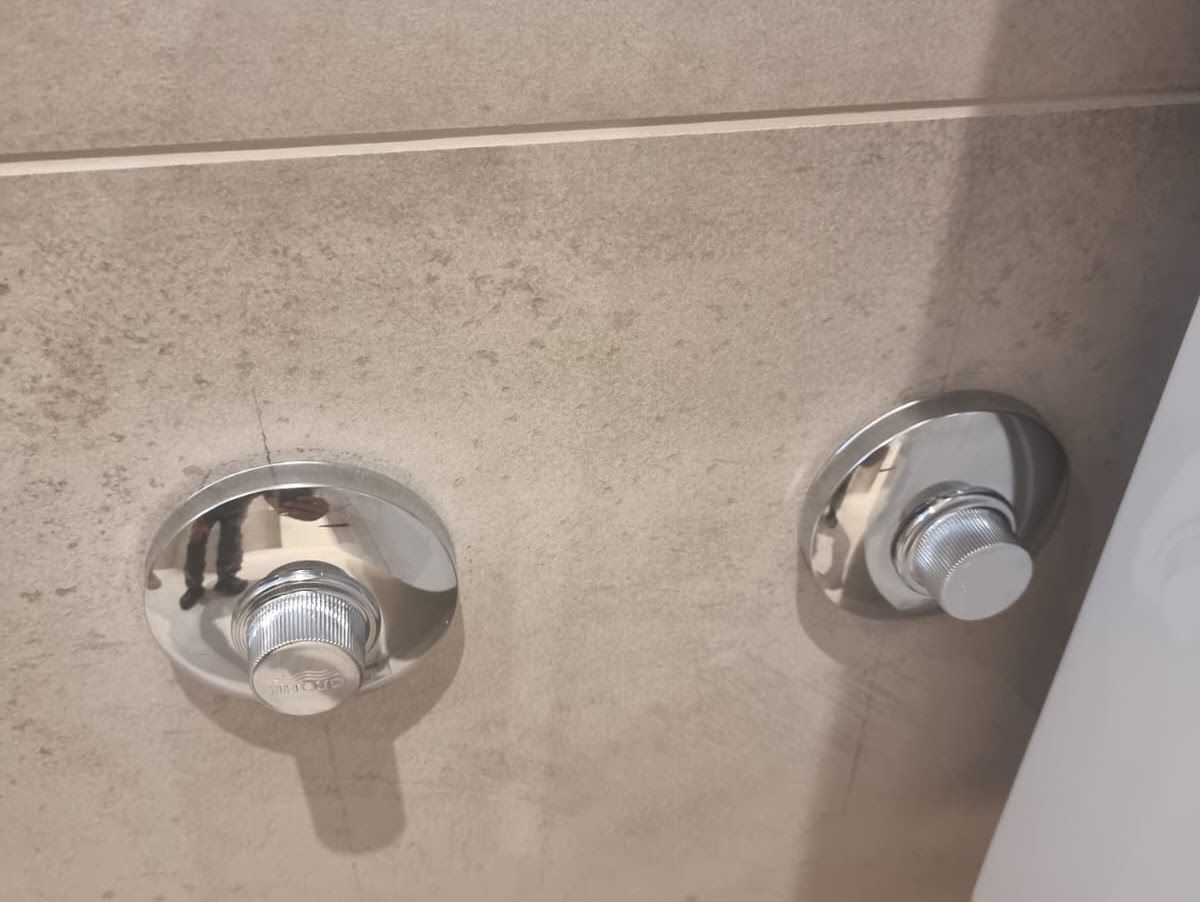 Zwei verchromte Einlasstaster an einer hellen, gefliesten Wand.