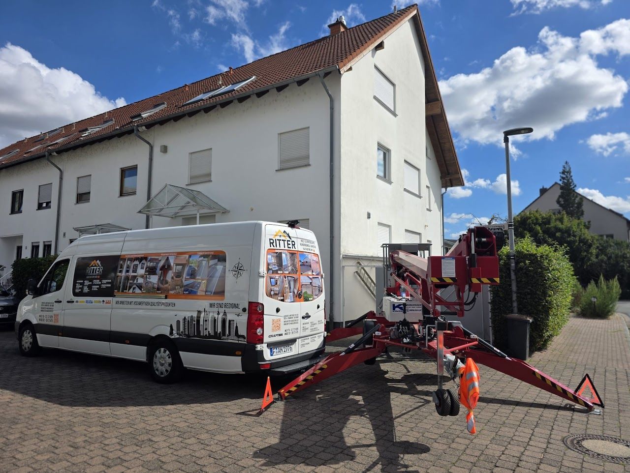 Weißer Lieferwagen mit Hebebühne in der Nähe eines Gebäudes, vermutlich für Bau- oder Instandhaltungsarbeiten.