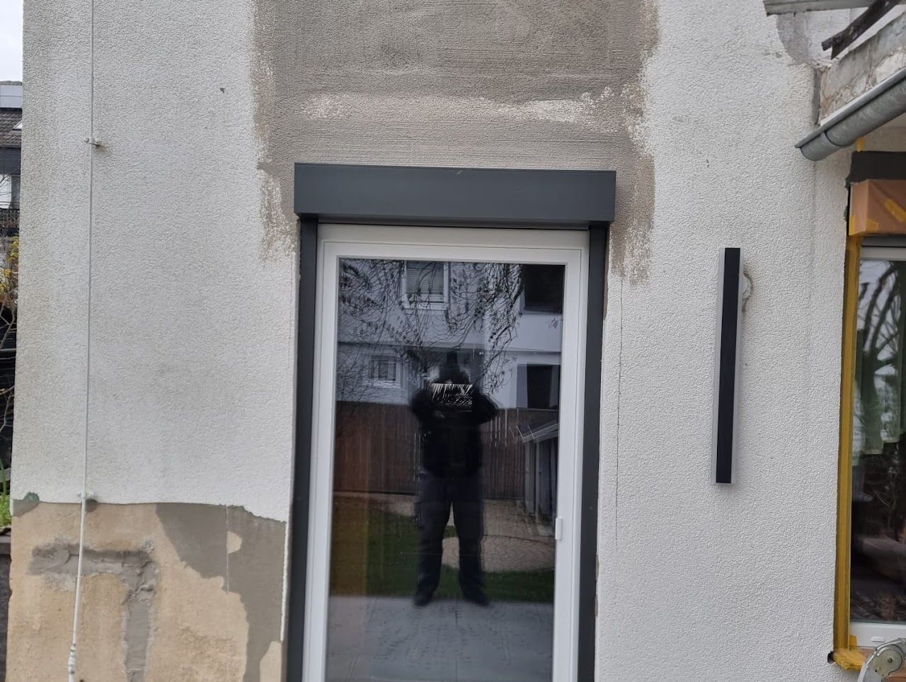 Eine Glastür mit grauem Fensterladen, die in eine Stuckwand eingelassen ist.