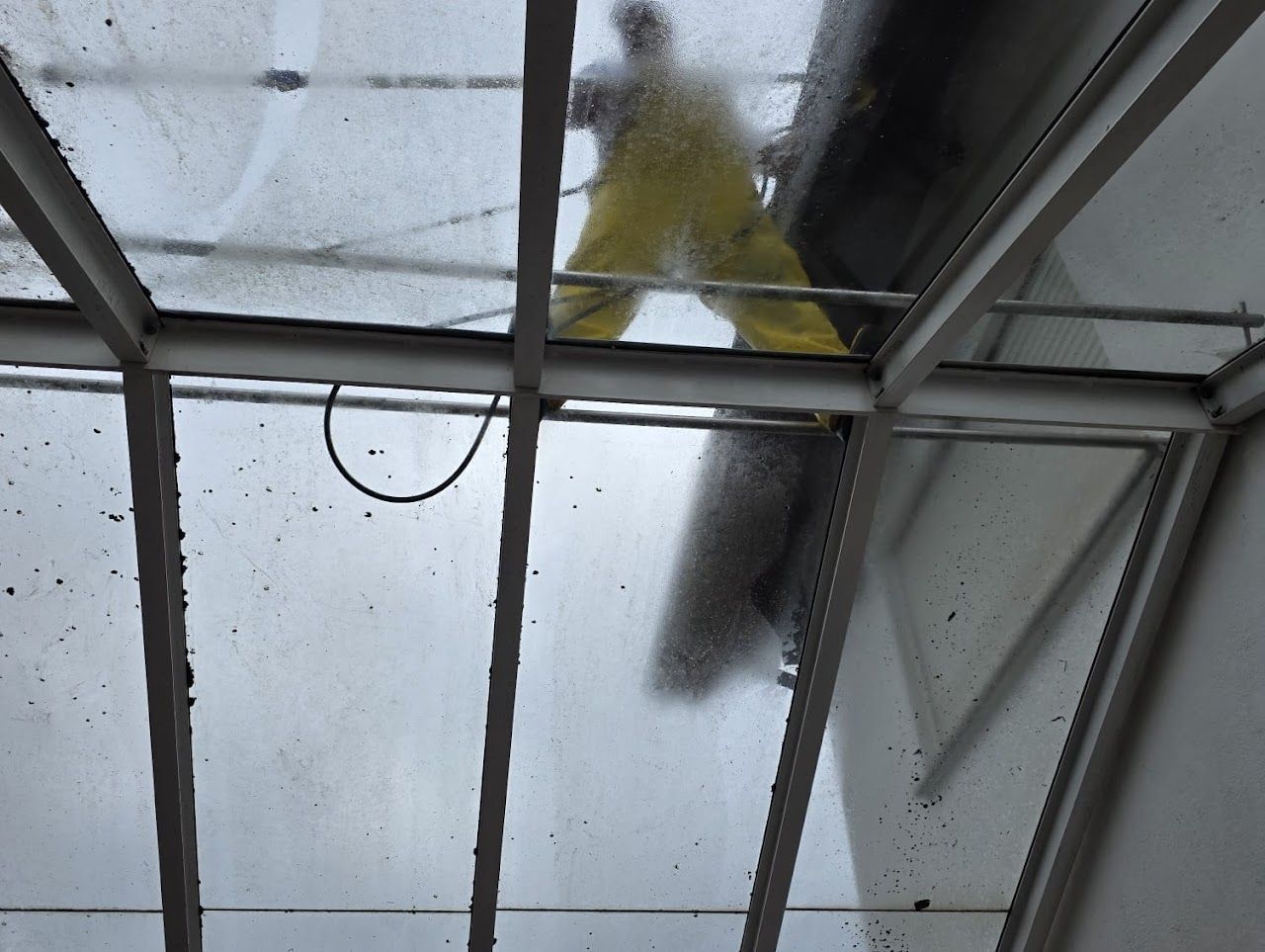 Eine Person in gelbem Anzug reinigt von oben ein Glasdachfenster.