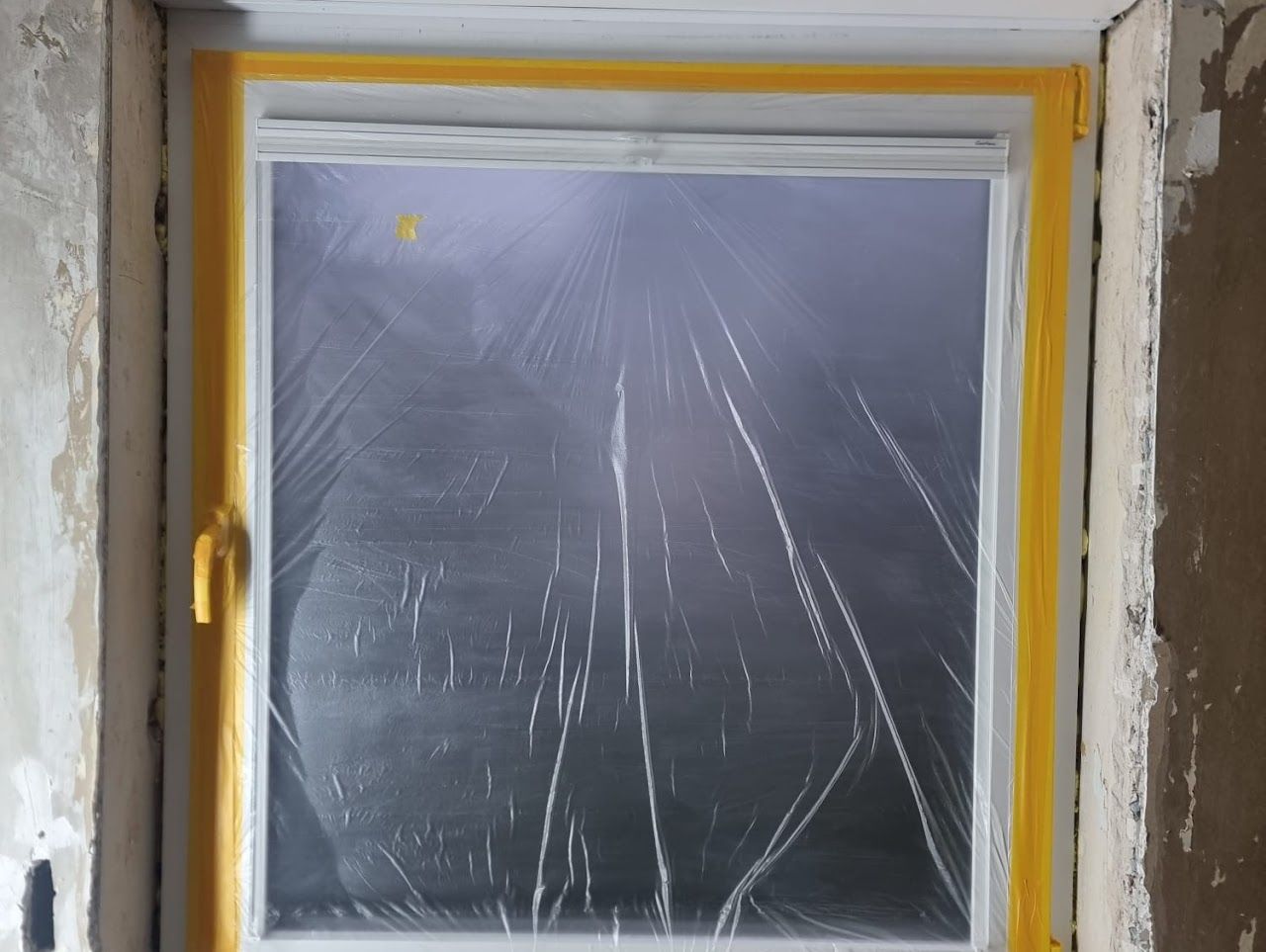 Ein mit Plastikfolie und gelbem Malerband verklebtes Fenster in einem im Bau befindlichen Gebäude.