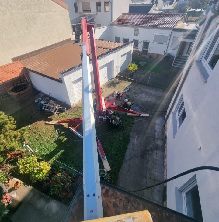 Eine Hubarbeitsbühne ragt über einen Wohngarten. Feuerwehrleute in roter Schutzausrüstung bedienen die Bühne.