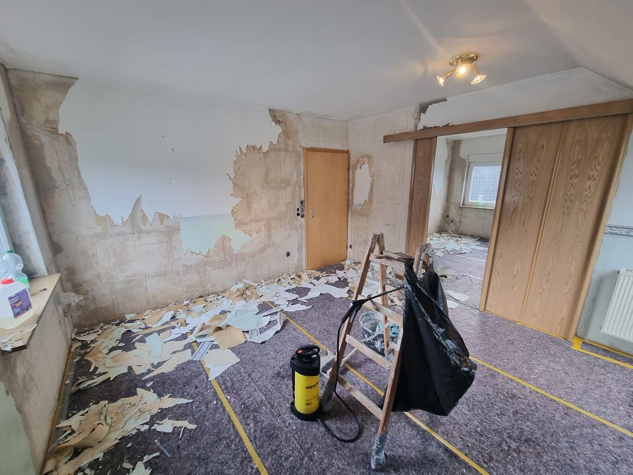 Zimmer wird renoviert: Tapeten werden entfernt, Bauschutt liegt auf dem Boden, Leiter, Staubsauger.