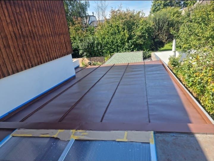 Braunes Metalldach auf einem Flachdach mit Kupferstreifen und teilweiser Abdeckung. Sonnige Außenlage.