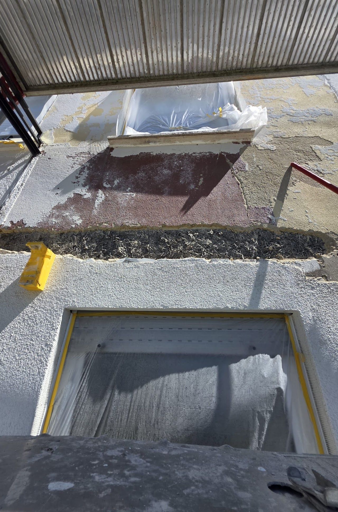 Außenwand mit zwei mit Plastikfolie abgedeckten Fenstern, Gerüst und teilweise fertiggestelltem Stuck.