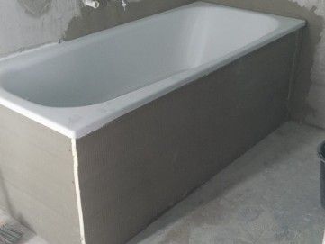 Eine Badewanne wurde in einem Badezimmer installiert; die Seitenwände sind unfertig grau, die Innenseite ist weiß.