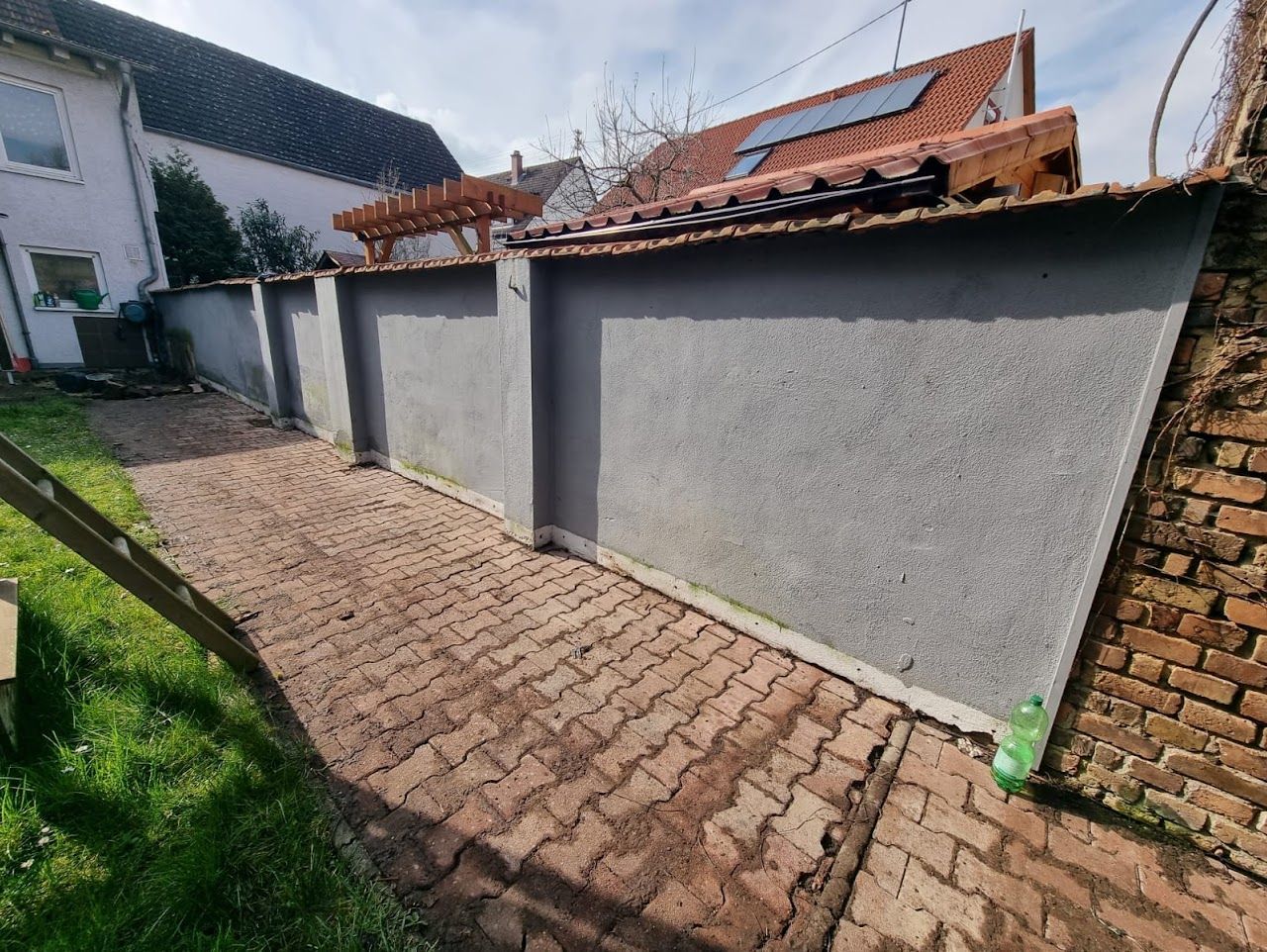 Ein von grauen Mauern und einem Backsteingebäude gesäumter Ziegelweg führt zu einem Garten.