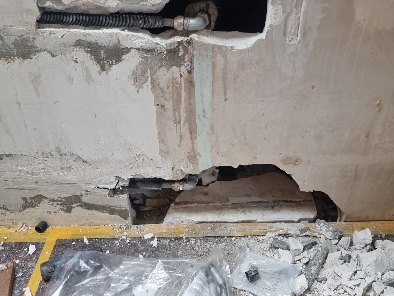 Freiliegende Rohre in einer Betonwand, wobei Teile der Wand abgebrochen sind.