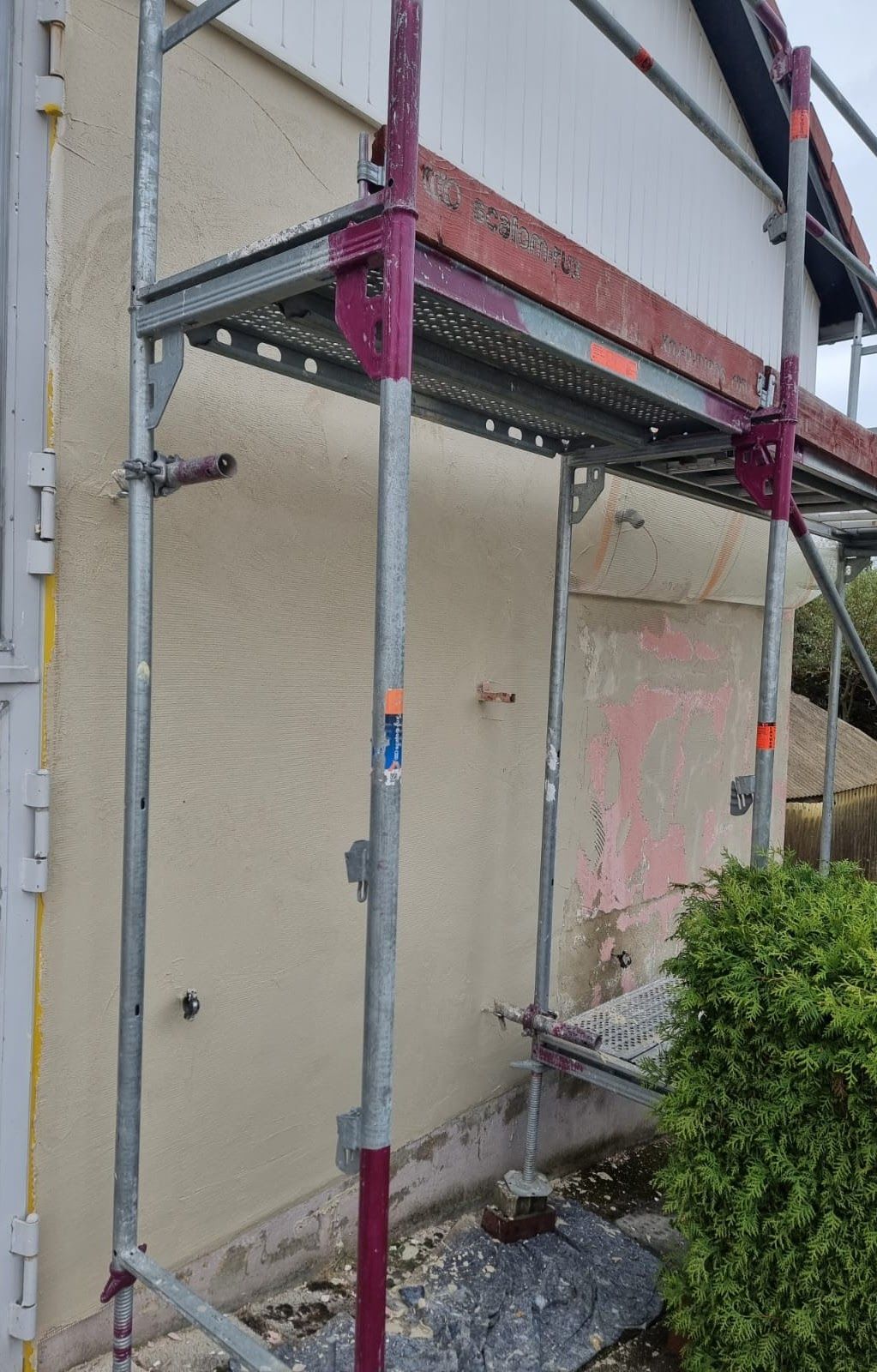 Gerüst an der Außenfassade eines Hauses, cremefarbene Wand mit sichtbaren Reparaturarbeiten.