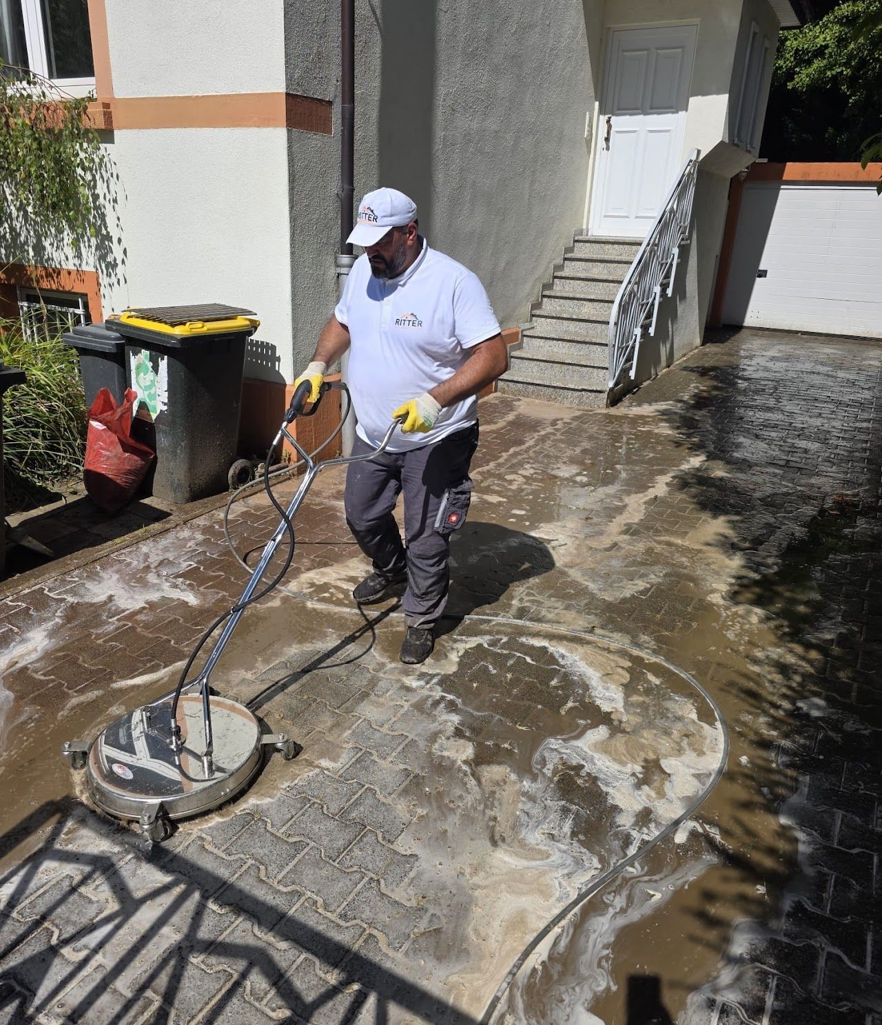 Ein Mann reinigt eine gepflasterte Auffahrt mit einem Hochdruckreiniger.