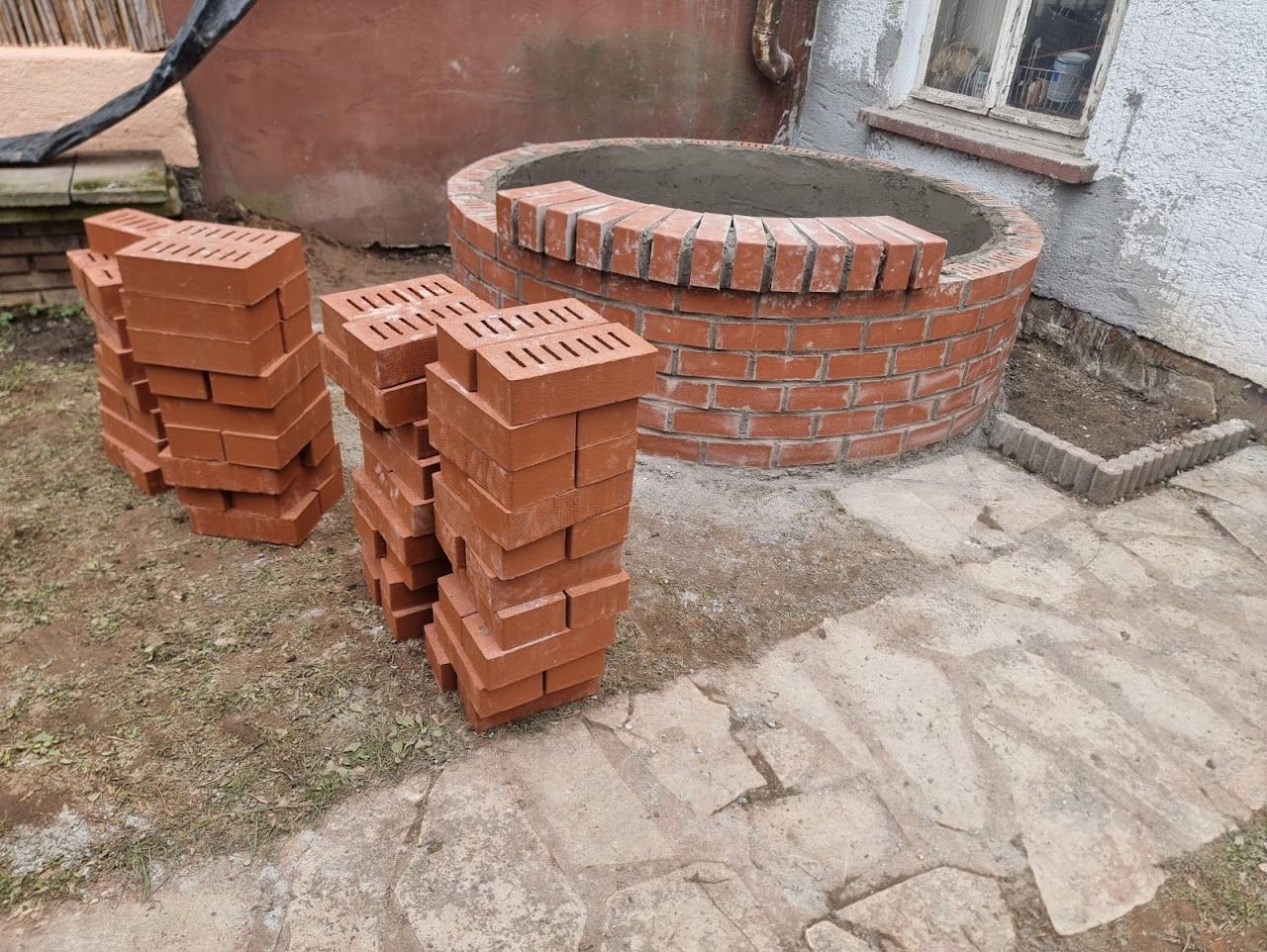 Stapel roter Ziegelsteine ​​in der Nähe eines im Bau befindlichen runden Ziegelbaus im Freien.