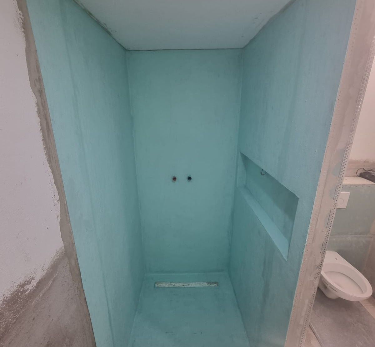 Neu gebaute Duschkabine, türkisfarbene Wände, Abfluss, Sanitärarmaturen, eingelassenes Regal. Badezimmer im Umbau.