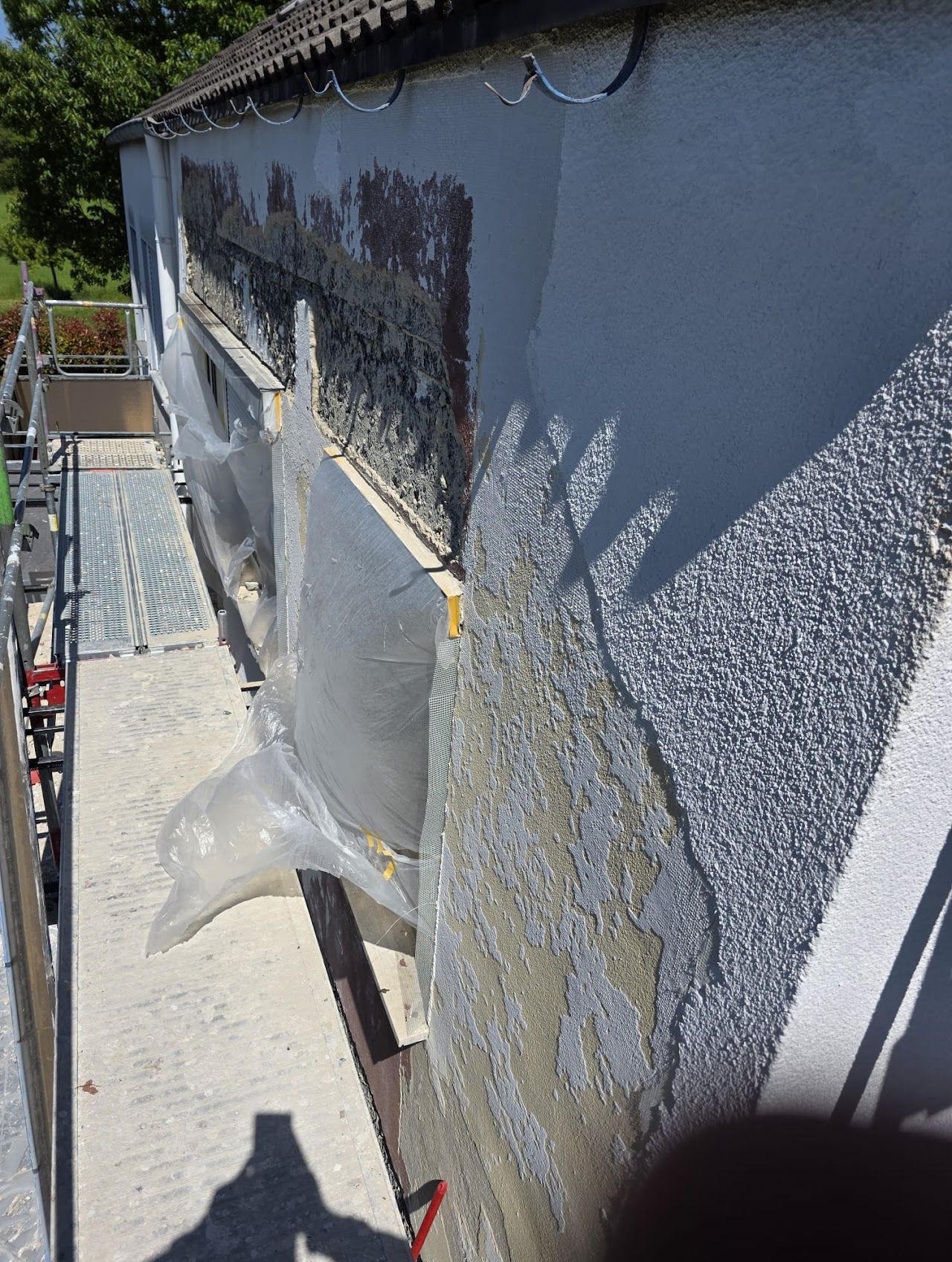 Außenansicht des Gebäudes mit Gerüst, freiliegendem Mauerwerk und Schutzfolie während der Reparaturarbeiten.