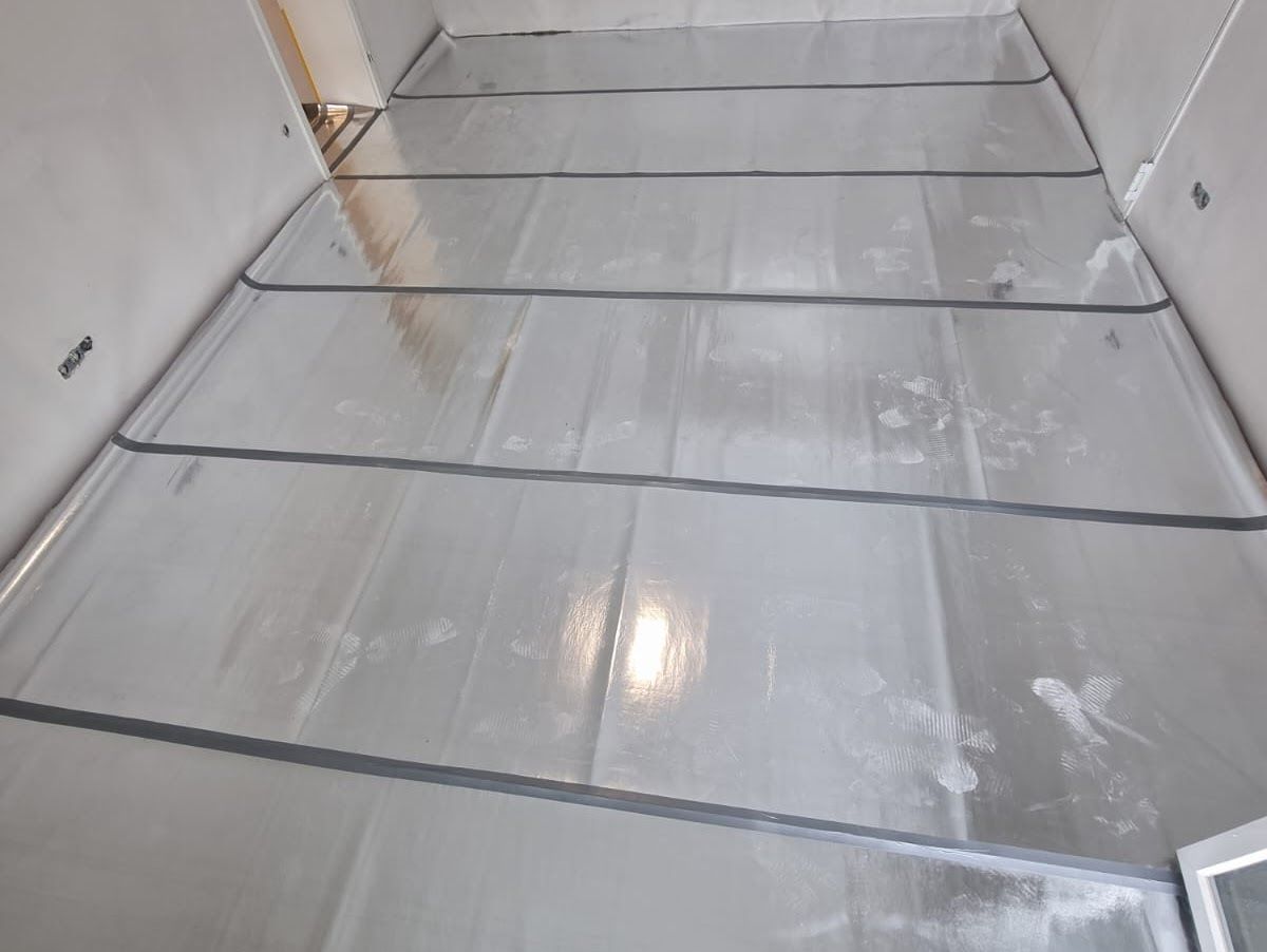 Grauer Fußboden mit dunklen Fugen in einem in Renovierung befindlichen Raum.