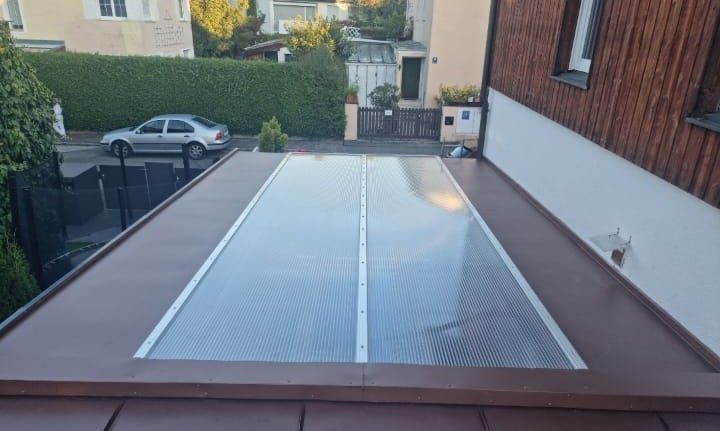 Ein Flachdach mit einer lichtdurchlässigen Platte in der Mitte. Im Hintergrund sind ein Auto und Gebäude zu sehen.