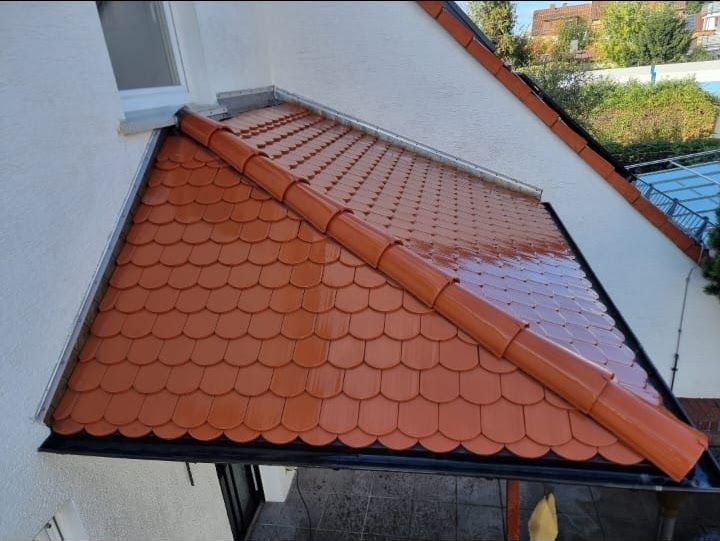 Orangefarbenes Ziegeldach mit Dachrinne und Fallrohr, Teil eines weißen Hauses.