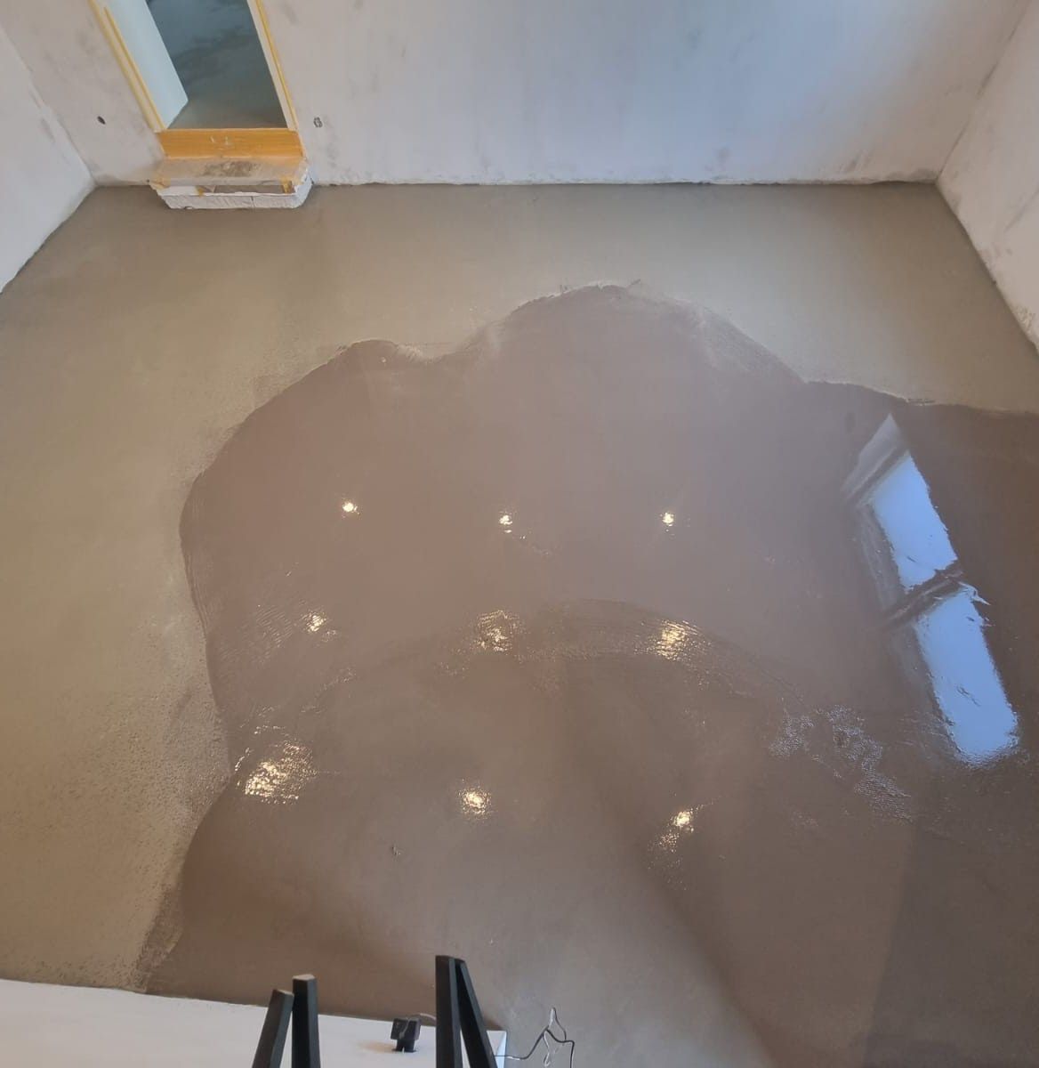 Raum mit frisch gegossenem, nassem, selbstnivellierendem Betonboden. Die Deckenleuchten spiegeln sich in der Oberfläche.