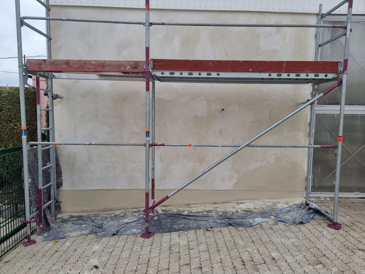 Ein Baugerüst steht neben einer Gebäudewand mit sichtbarem Putz.