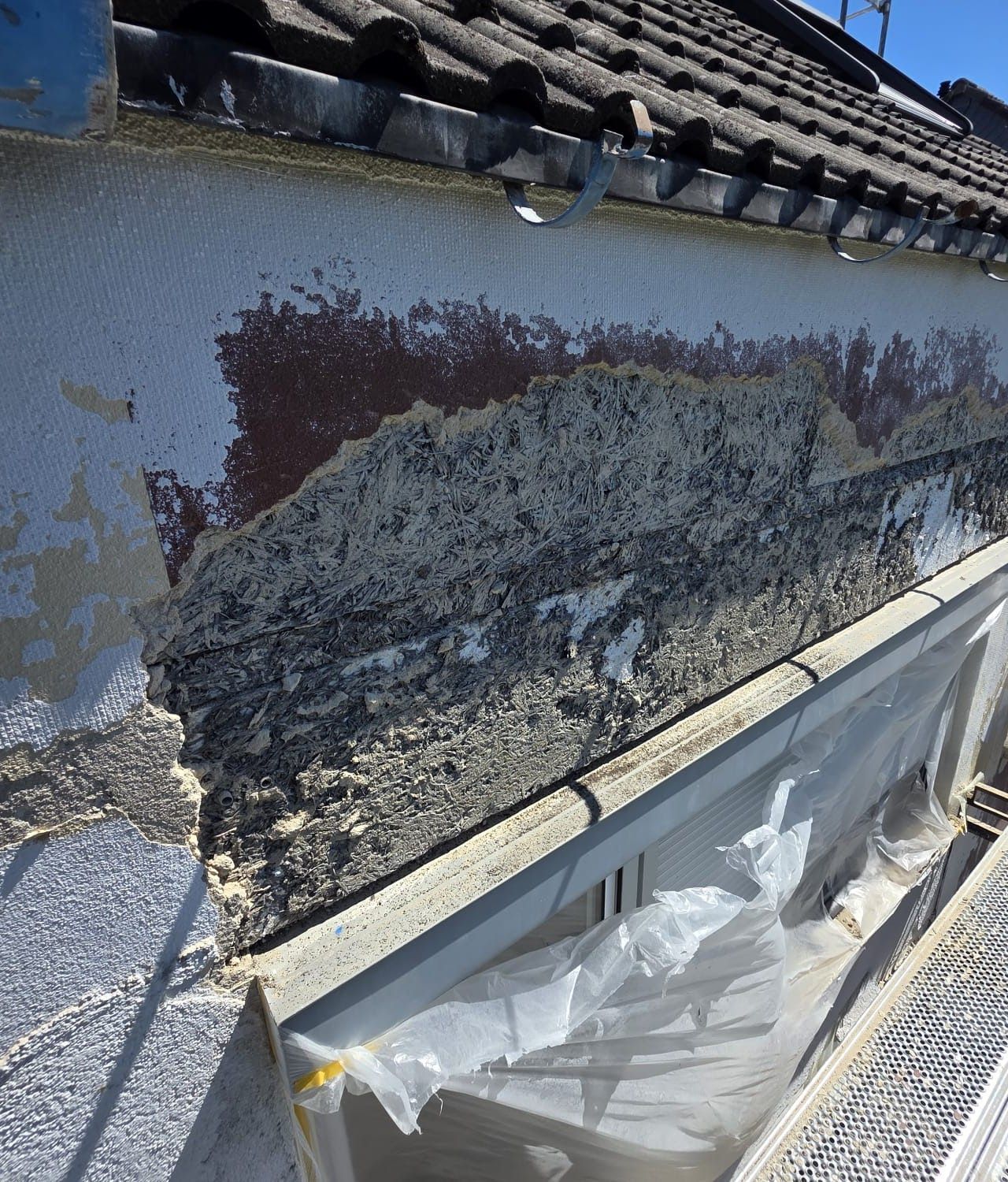 Außenwand mit abblätternder Farbe und möglichen Wasserschäden in der Nähe von Dach und Dachrinne.