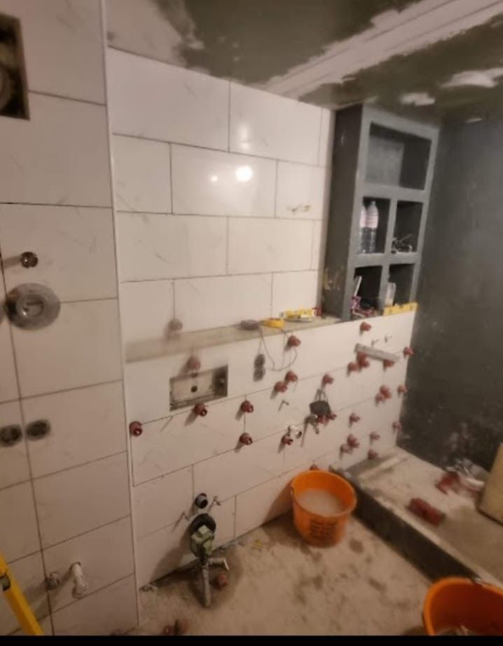 Badezimmer im Bau, geflieste Wände, Einbauregale, Sanitärarmaturen, orangefarbener Eimer.