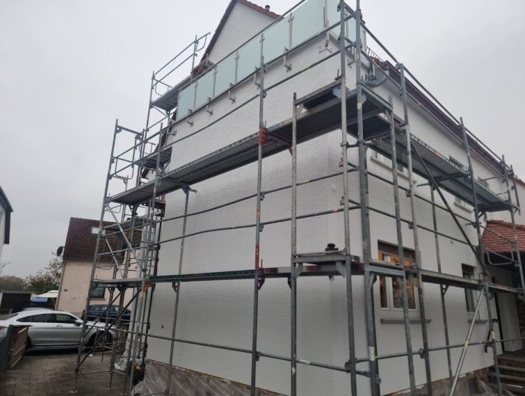 Ein zweistöckiges weißes Gebäude mit rotem Ziegeldach ist von einem Gerüst umgeben; der Himmel ist bewölkt.