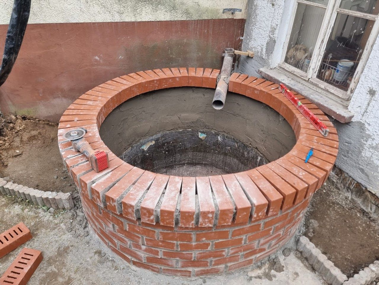 Mit Ziegeln ausgekleideter Brunnen mit kreisförmigem Ziegelrand, unfertig, mit Werkzeugen an der Seite.