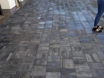 Dunkelgraue Ziegelsteine ​​auf einem Gehweg, auf dem die Beine und Füße einer Person sichtbar sind.