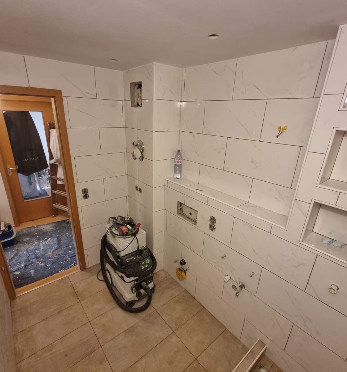 Das Badezimmer wird renoviert; Wände und Boden sind gefliest, Armaturen sind installiert und Werkzeuge sind vorhanden.
