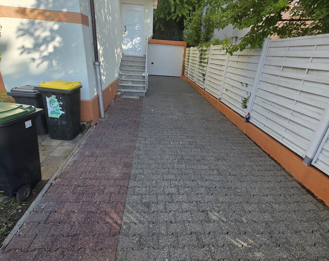 Eine mit Pflastersteinen belegte Auffahrt, die von einem weißen Zaun und Gebäude mit orangefarbenen Verzierungen gesäumt ist.
