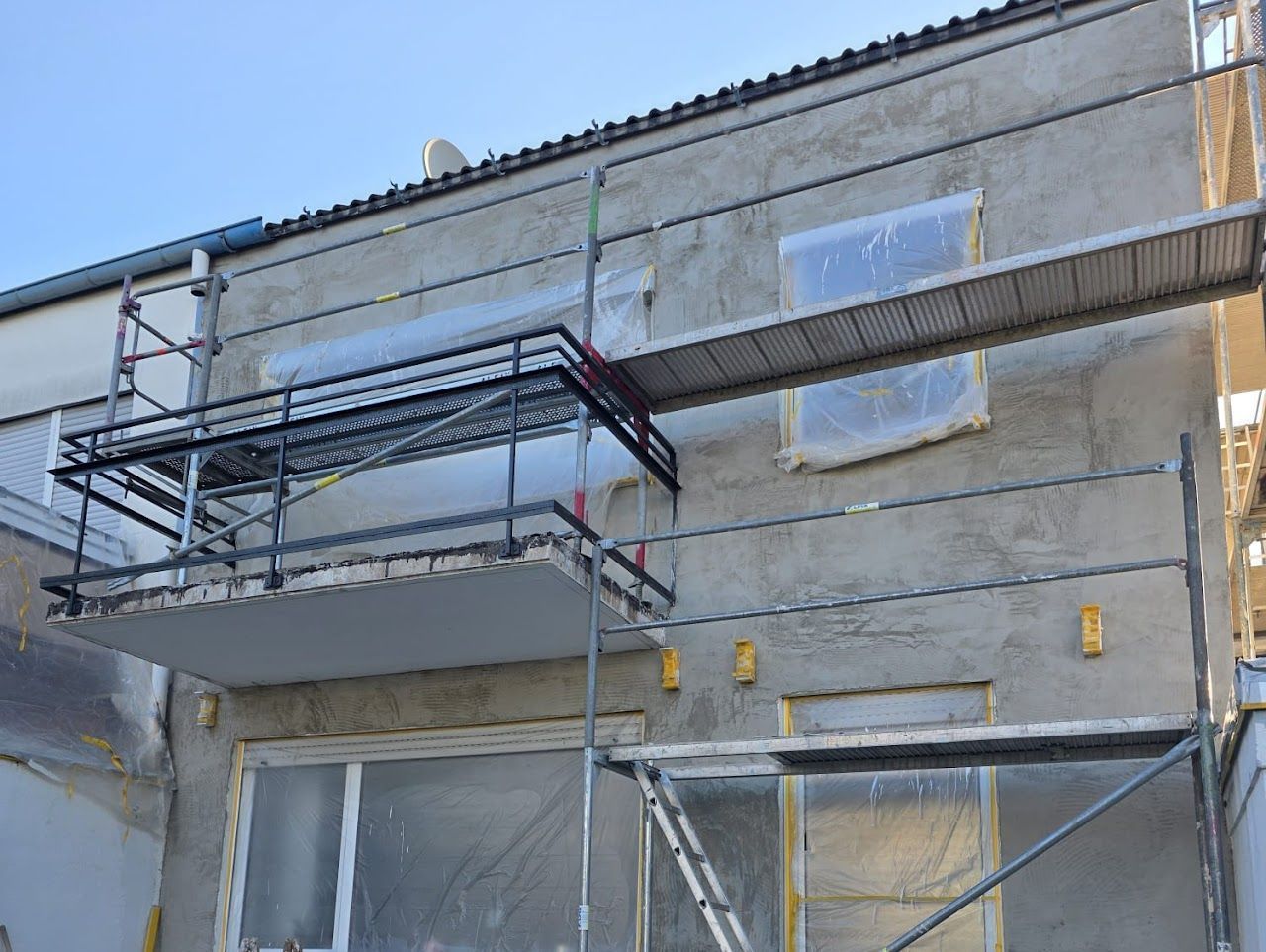 Außenansicht eines Gebäudes, das renoviert wird, mit Gerüst und Schutzfolien an den Fenstern.