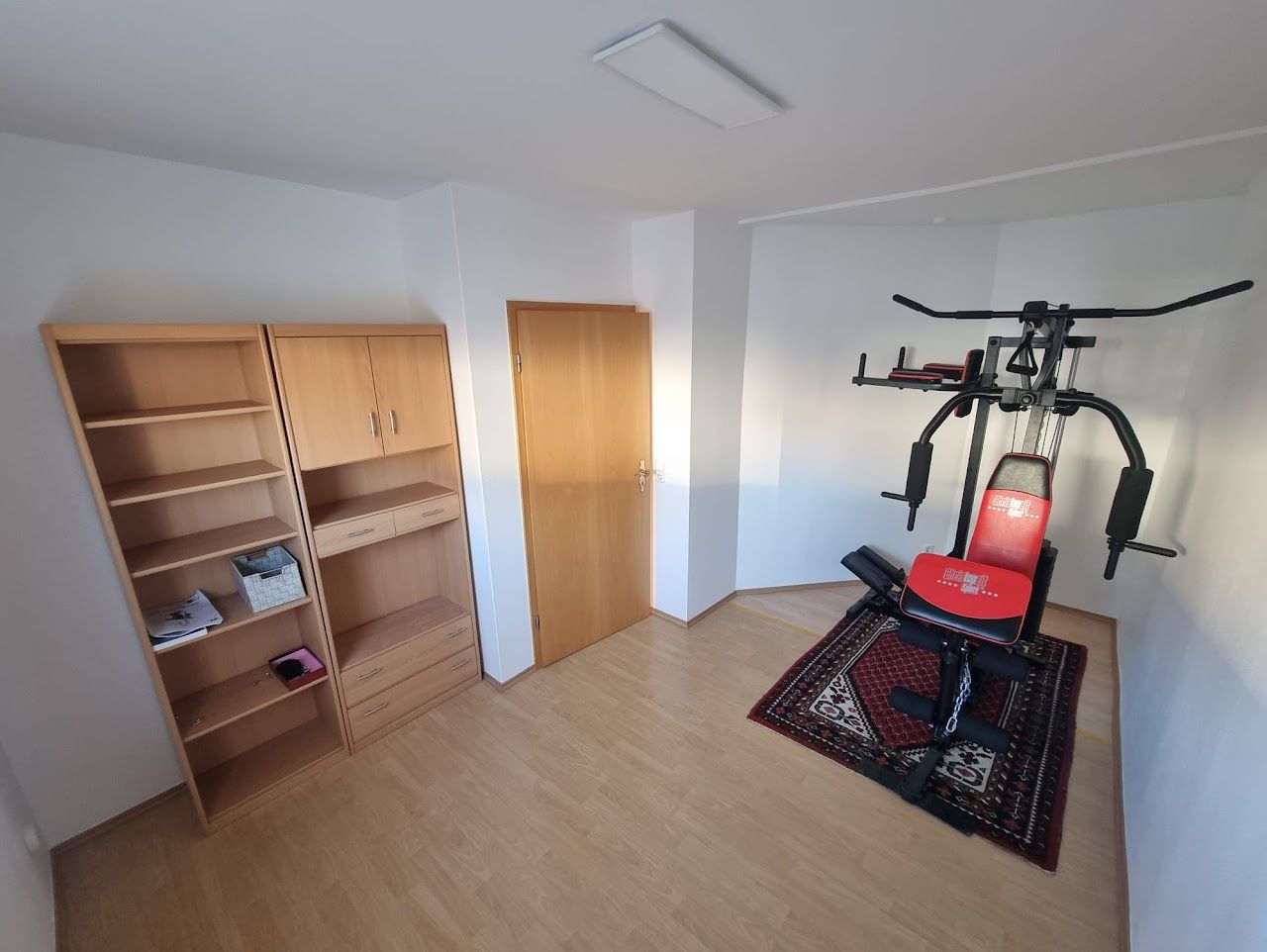 Heim-Fitnessstudio mit Krafttrainingsgeräten, Bücherregalen und geschlossener Tür auf Holzboden.