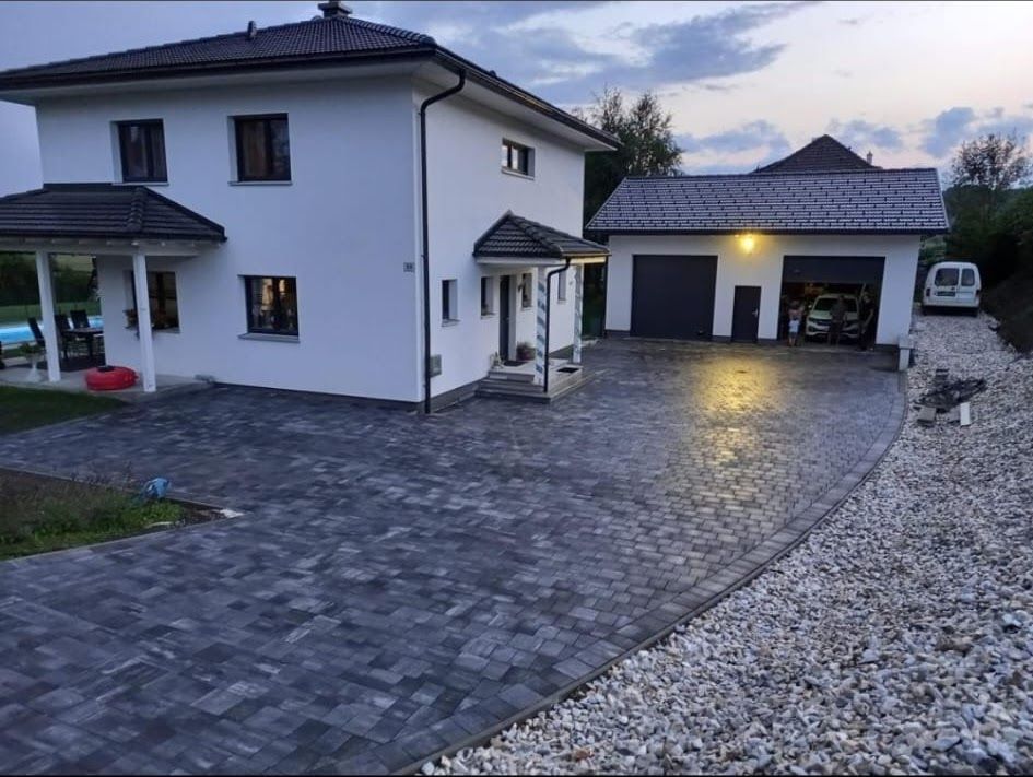 Zweistöckiges weißes Haus mit gepflasterter Auffahrt, die zu einer Garage führt. Bewölkter Himmel.