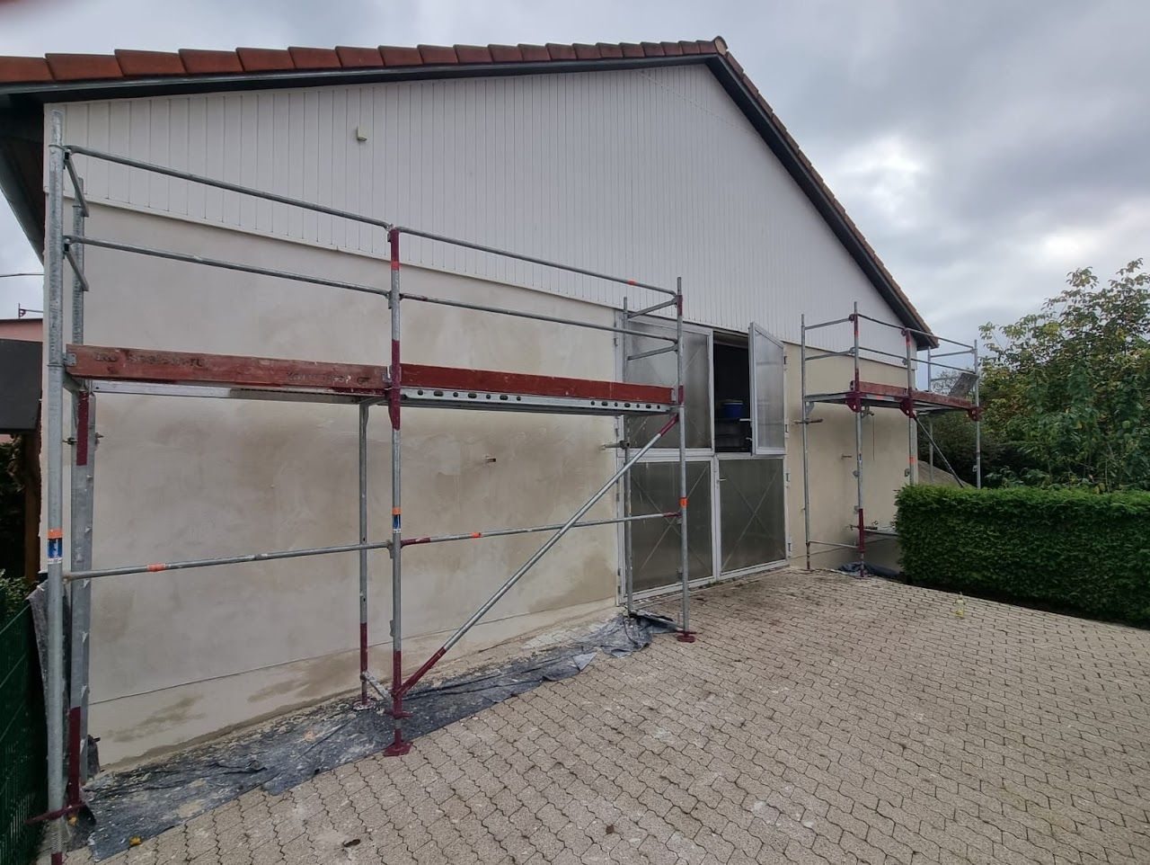 An einem Haus mit weißer Fassade, neben einer Kiesauffahrt, wurde ein Gerüst errichtet.