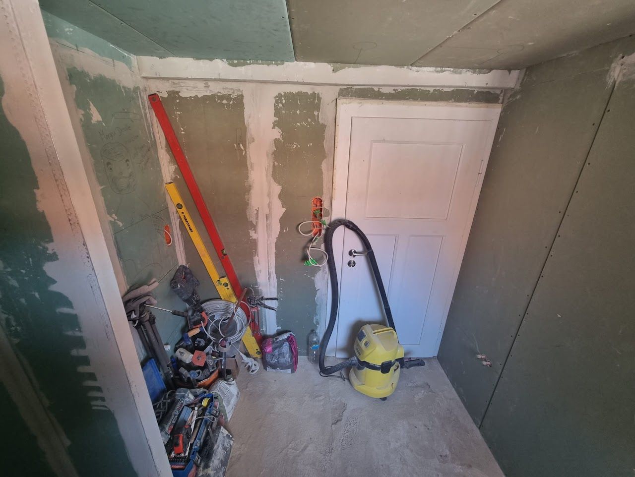 Innenausbau: Trockenbauwände teilweise montiert, Werkzeug und Staubsauger vorhanden, Tür am Ende.