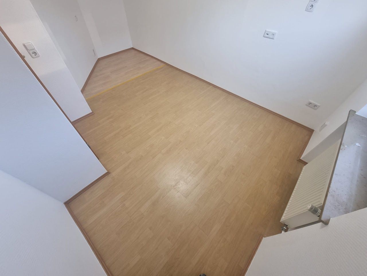 Leerer Raum mit hellen Holzböden und weißen Wänden.