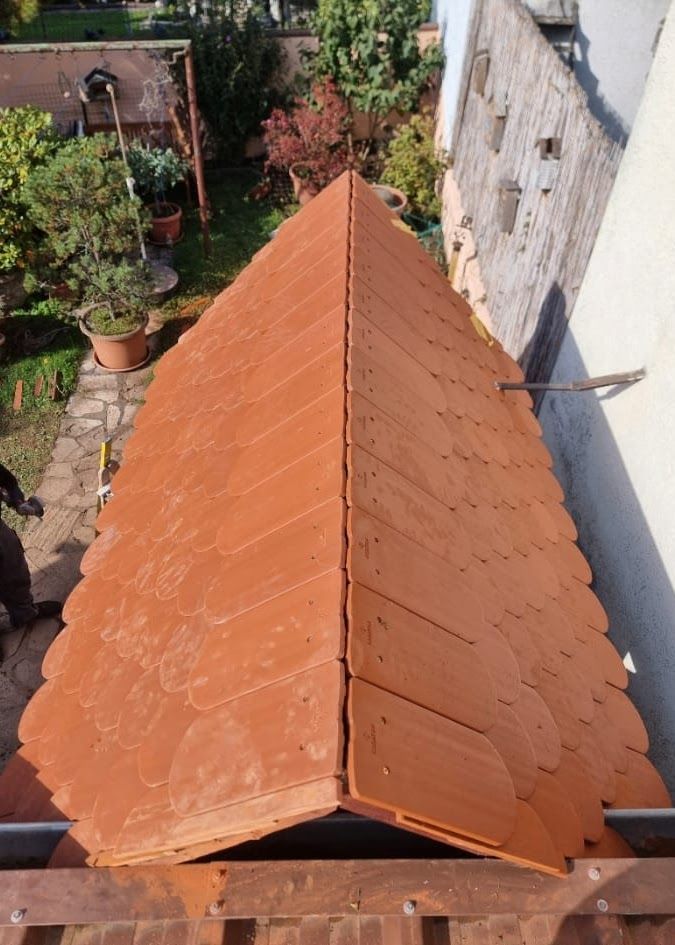 Ein Dach aus roten Tonziegeln wird verlegt; die Bauarbeiten finden im Freien statt.