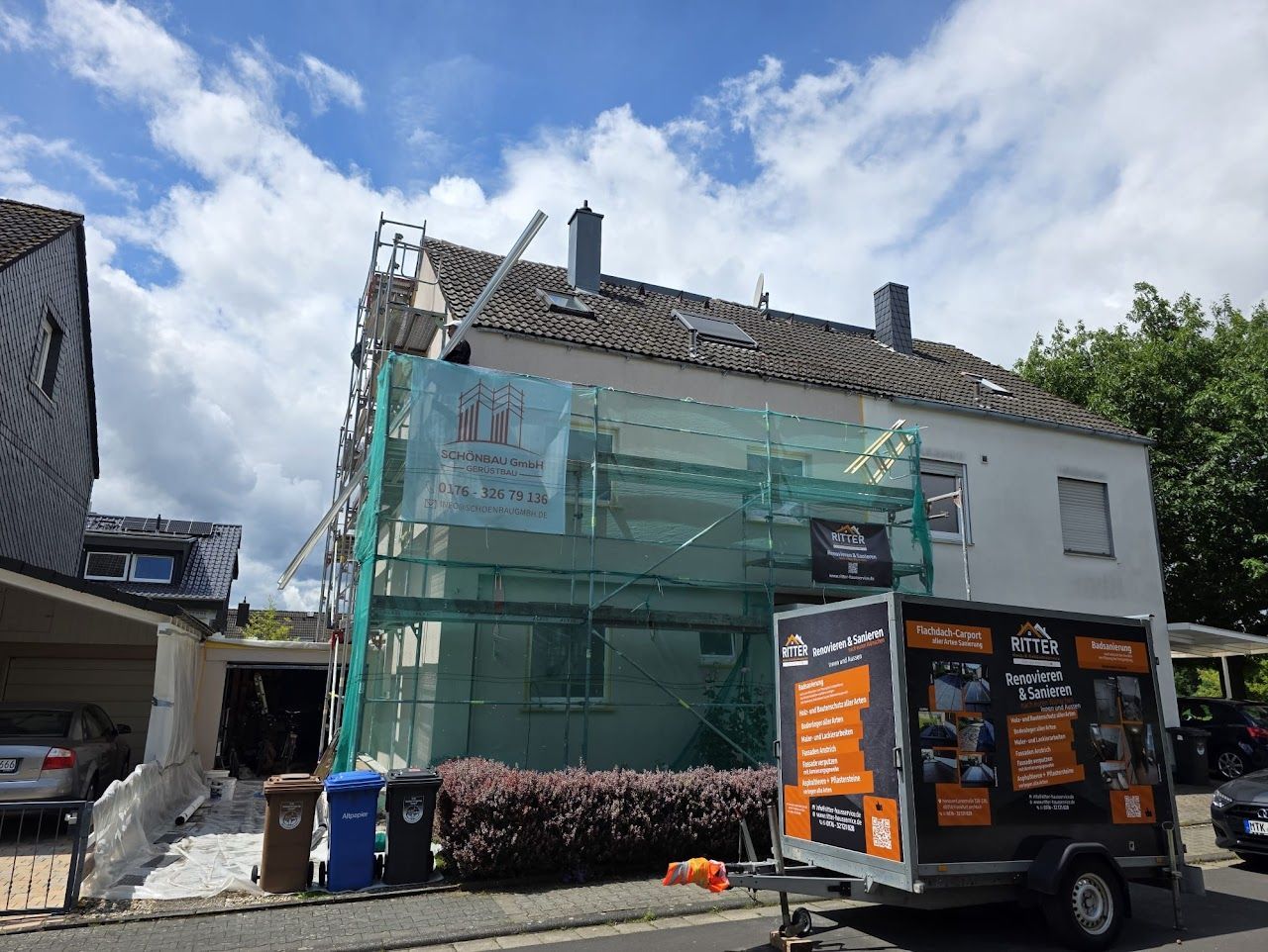 Haus mit Gerüst und Anhänger; Dachreparatur im Gange. Bewölkter Himmel.