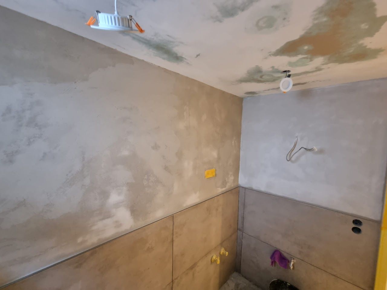 Badezimmerinnenraum mit unfertigen Zementwänden und -decke, elektrischen Installationen und freiliegenden Kabeln.