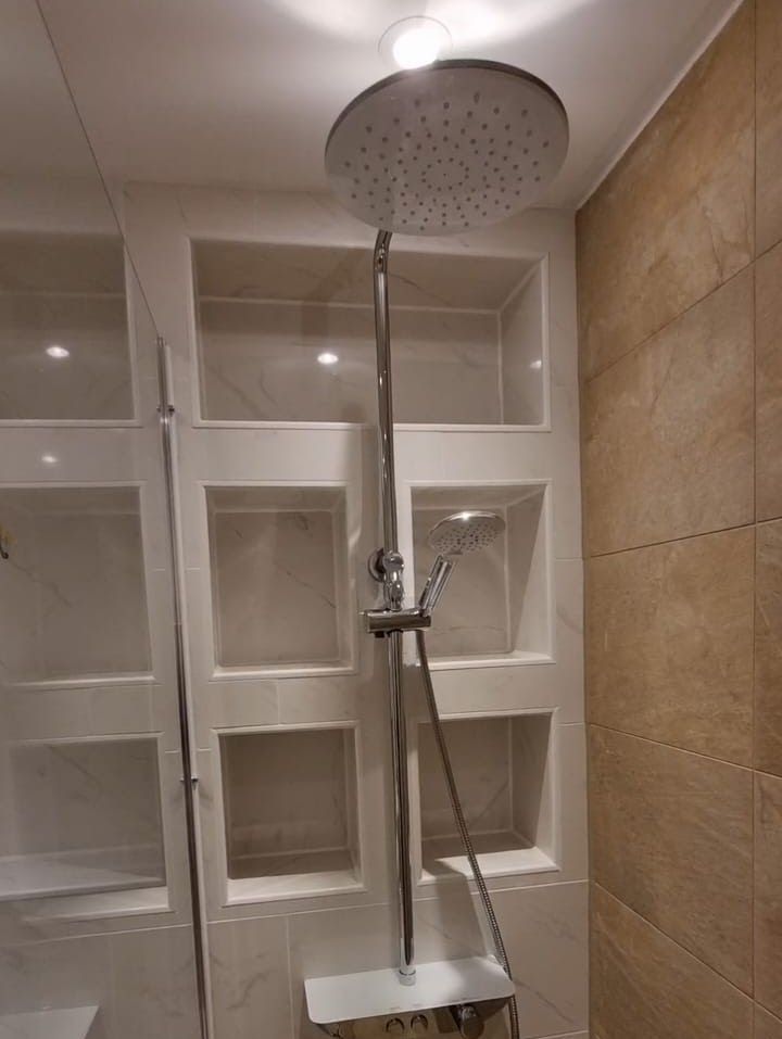 Dusche mit großem Regenduschkopf, integrierten Ablagen und Handbrause. Fliesen in hellen und dunklen Tönen.