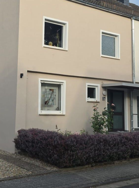 Beiges zweistöckiges Haus mit blauem Garagentor, Kiesauffahrt und kleiner Hecke im Vorgarten.