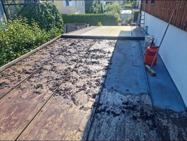 Ein Flachdach, auf dem Schutt entfernt wird; Propangastank und Besen sind zu sehen.