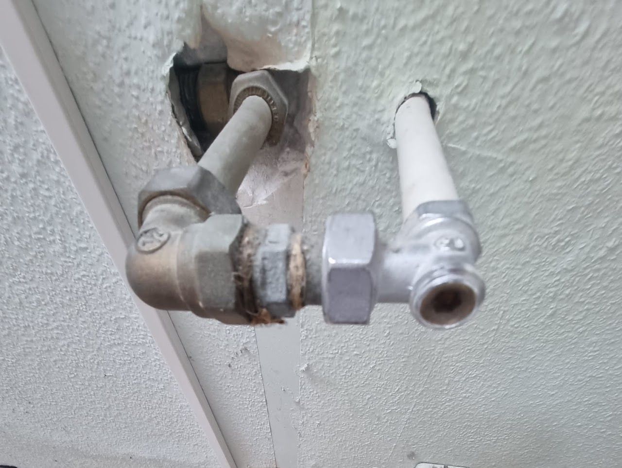 Sanitärrohre und Ventil in der Decke installiert; Armaturen aus Messing und Silber, weißes Deckenmaterial.