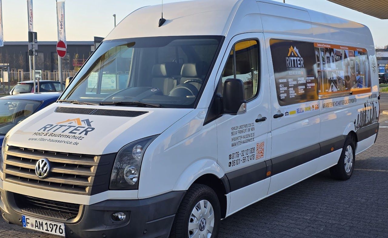 Ein weißer Volkswagen-Transporter mit dem Logo „Ritter Reisen“ parkt, möglicherweise an einer Tankstelle.